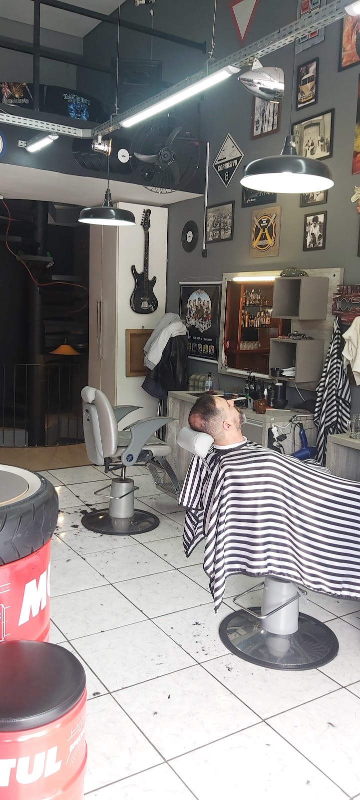 Cliente sendo atendido na cadeira de barbeiro, com guitarra e pôsteres de rock na parede